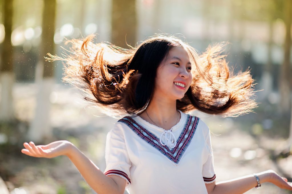 Cheerful young woman with flowing hair smiling in a sunny park setting.