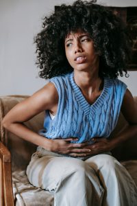 African American woman in pain due to stomach cramps indoors. Health and wellness concept.