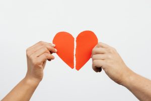 A close-up view of hands holding a torn red paper heart, symbolizing heartbreak or relationship issues