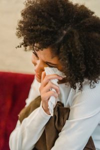 Woman experiencing a moment of sadness, wiping tears with a tissue while sitting on a cozy couch.