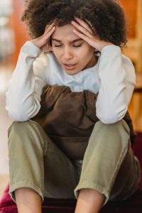 Woman sitting indoors with a stressed expression holding her head