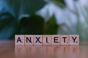 Close-up of wooden blocks spelling ANXIETY on a wooden surface with blurred green background