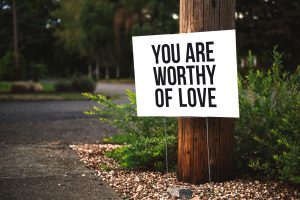 A positive message sign "You are worthy of love" in a park setting