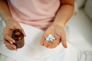 Close-up of an adult taking medication with blue pills in hand, promoting health recovery at home.