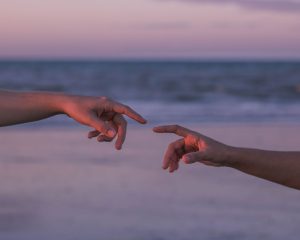 Two hands reaching towards each other on a beach during a serene sunset, evoking connection and tranquility.