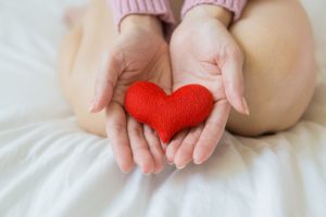 Soft focus on hands holding a red heart, symbolizing wellness and care in a serene setting.