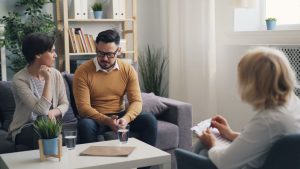 A couple engaged in a counseling session with a therapist in a cozy room.