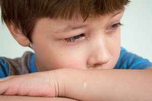 A young boy with a tear on his face, looking pensive and sad. 