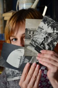 Close-up of a woman holding vintage black and white photos, partially obscuring her face. 